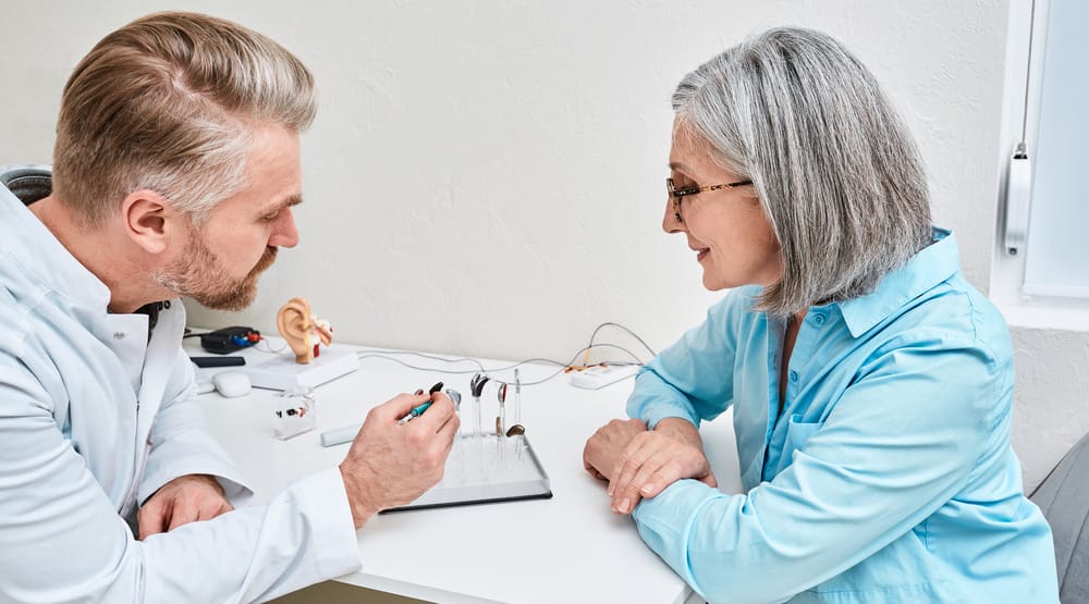 Male audiologist and female patient discussing hearing aid models.