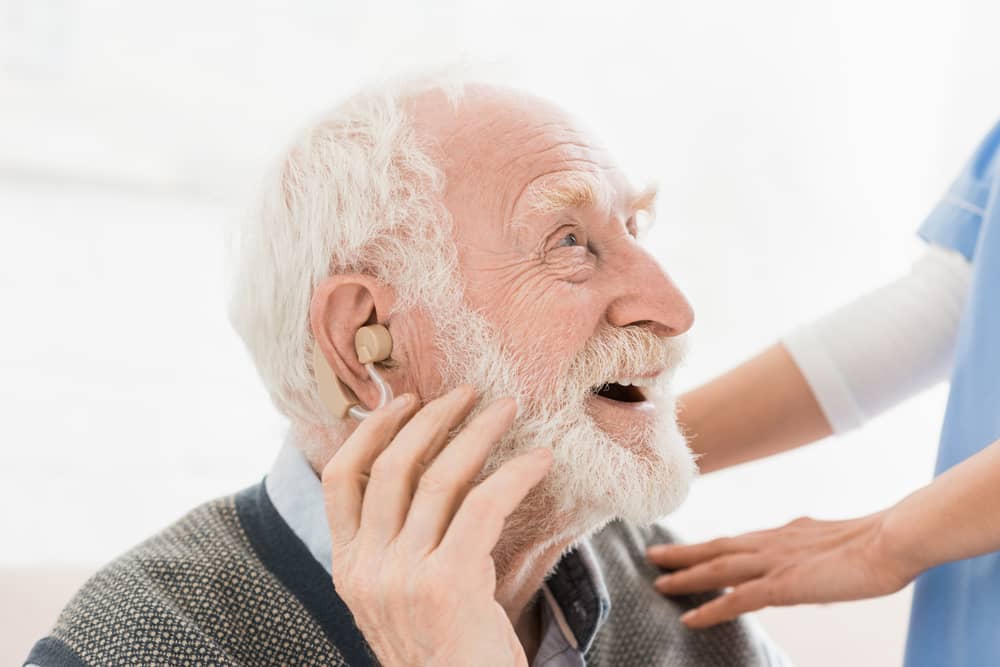 Elderly man having hearing aid fitted, smiling