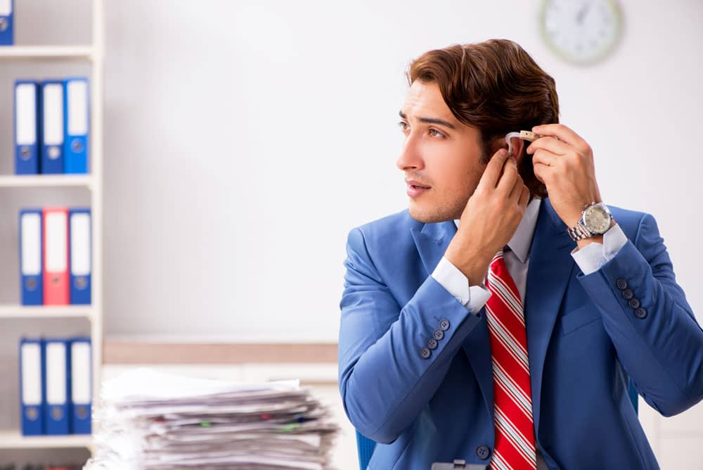 Male employee in office environment inserting a hearing aid in his ear