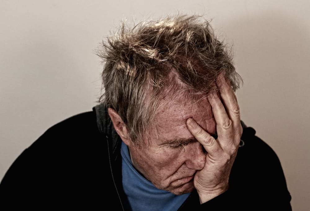 Distressed elderly man covering face with hand