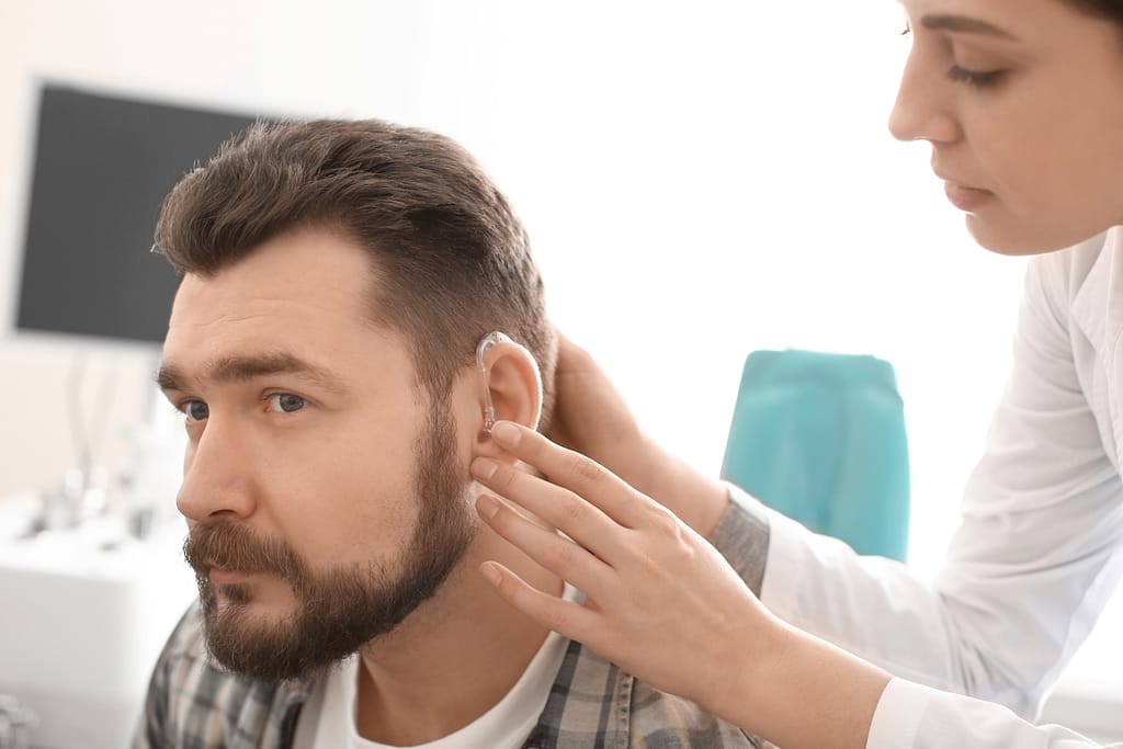 Otolaryngologist putting hearing aid in man's ear in hospital