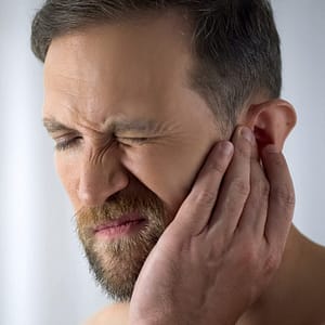 Man holding his hand up to his ear, grimacing as if in pain