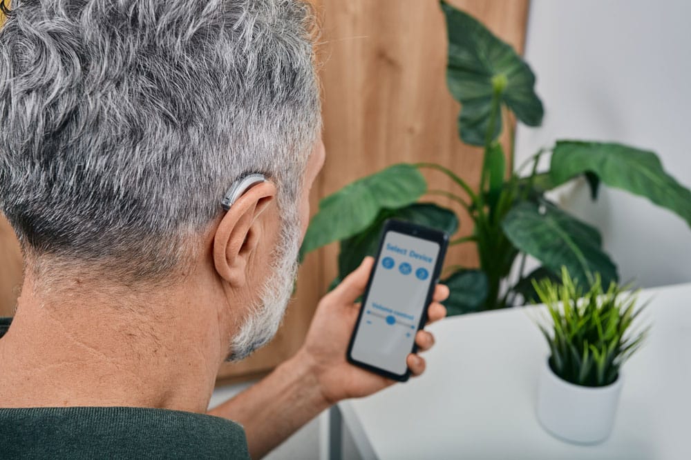 Senior man wearing hearing aid adjusting device's settings on his phone