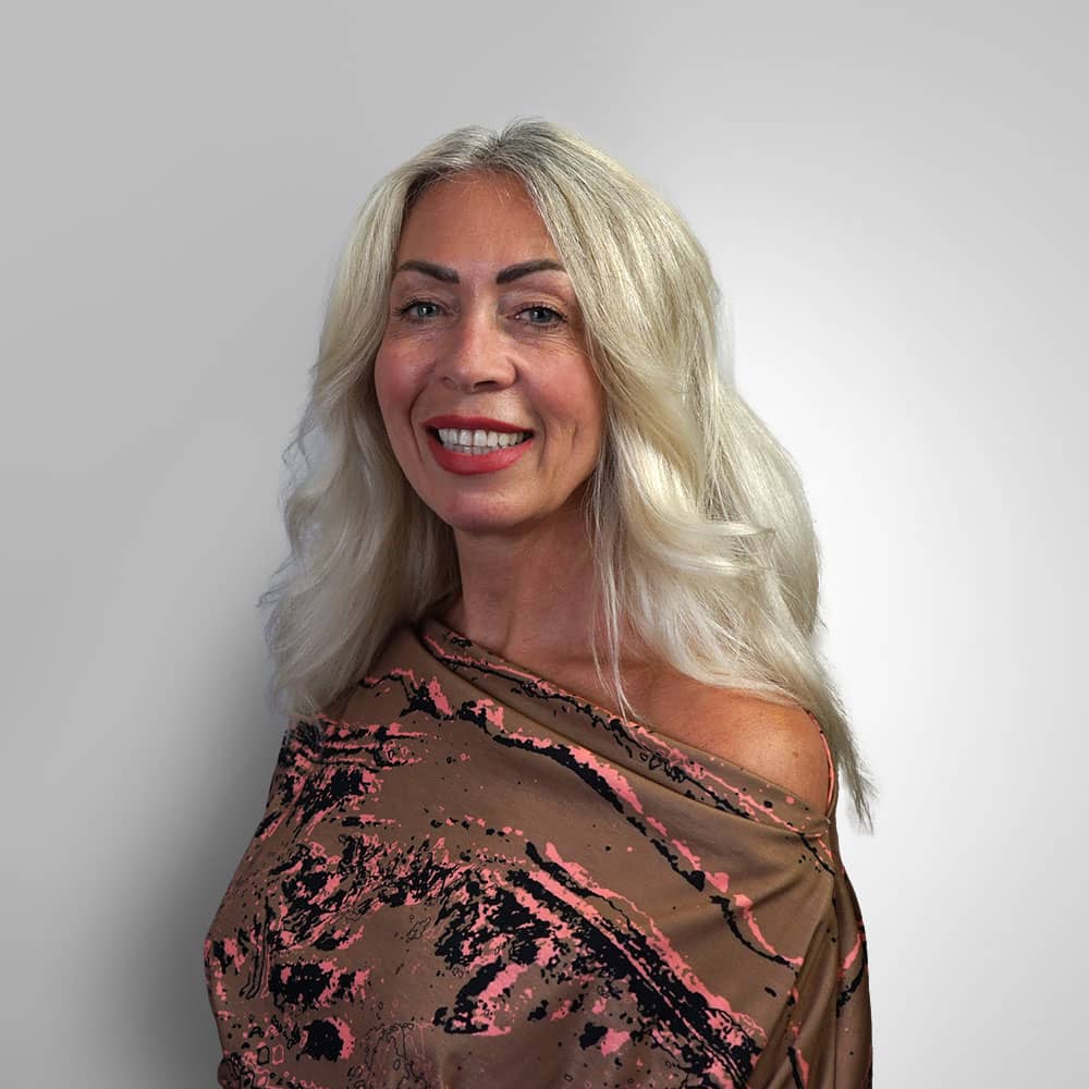 Photograph of Hear4U CEO Samantha Bennett with silver hair, wearing brown dress with pink flowers on grey background