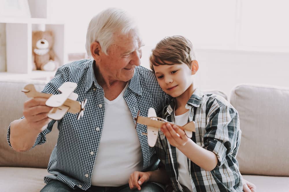 Old gentleman playing with grandchild using wooden airplanes