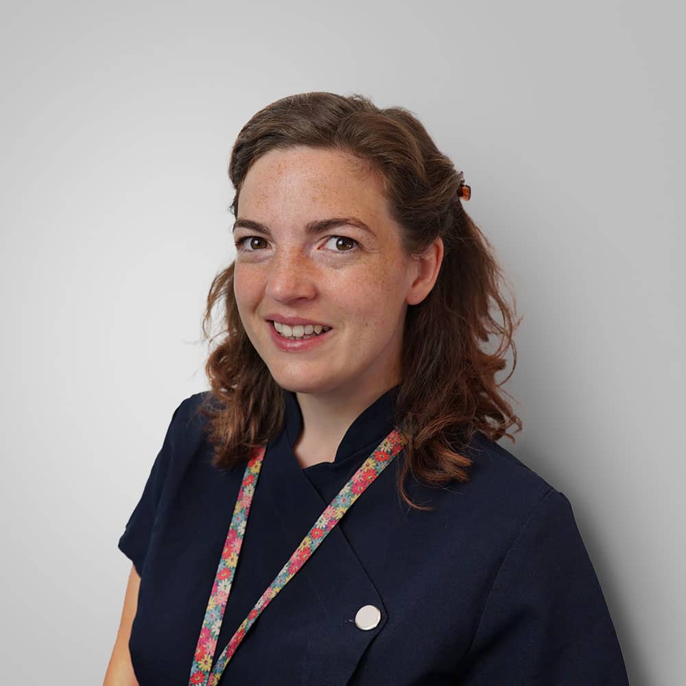 Photograph of female audiologist (Rosie) in navy clothes and with a flower staff ID lanyard