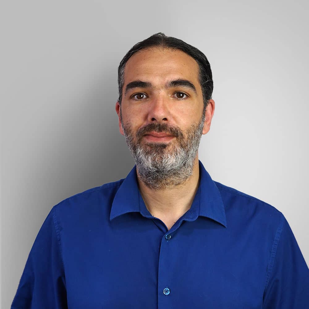 Photograph of audiologist (Ben Bennett) wearing blue shirt whilst smiling with black short cut hair and silver beard