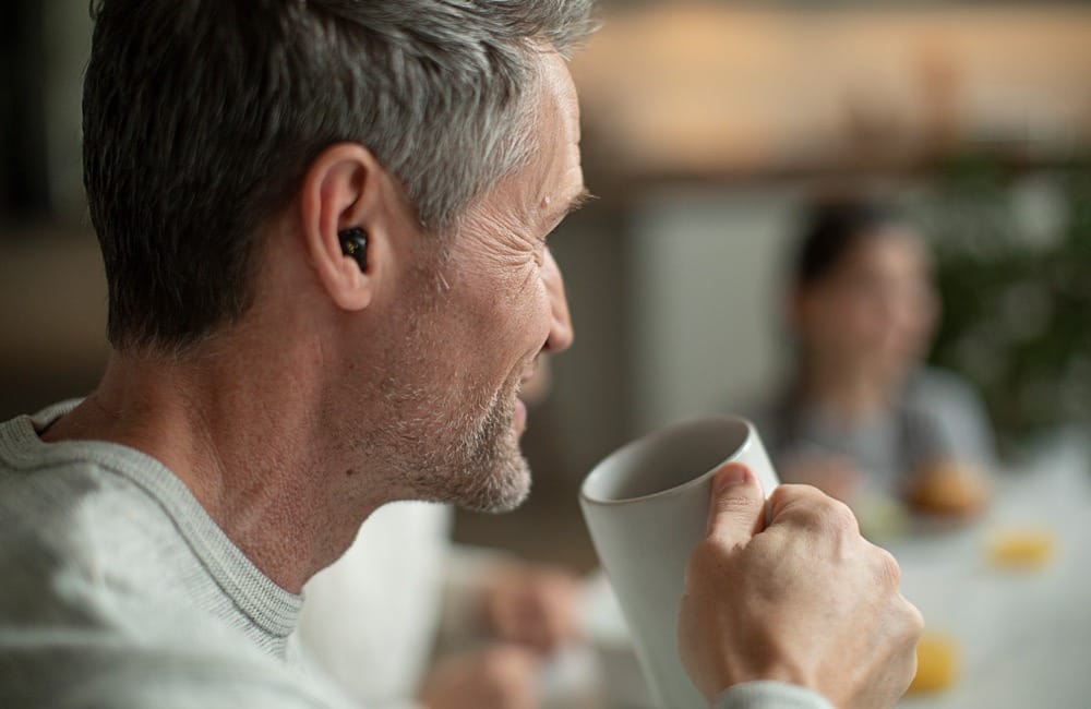 Photograph of man sitting in cafe with hearing aids in ear