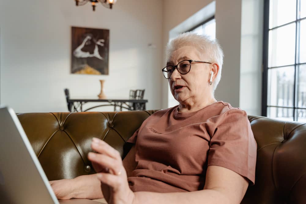 Elderly lady sitting on brown sofa with laptop on lap