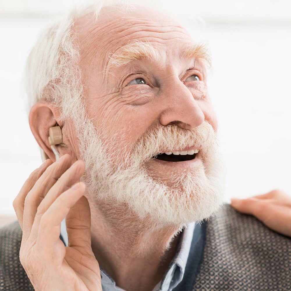 Elderly man looking up smiling with hearing aid sticking out of his ear with white background