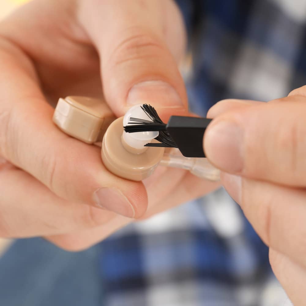 Extreme closeup of hands cleaning a hearing aid with a specialised brush
