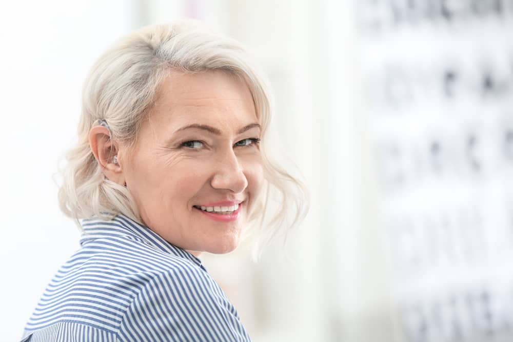 Elderly woman wearing hearing aid looking at camera, smiling