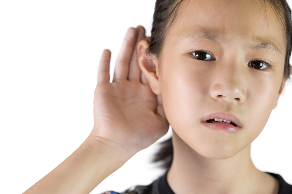 Young girl holding hand up to her ear visibly struggling to hear