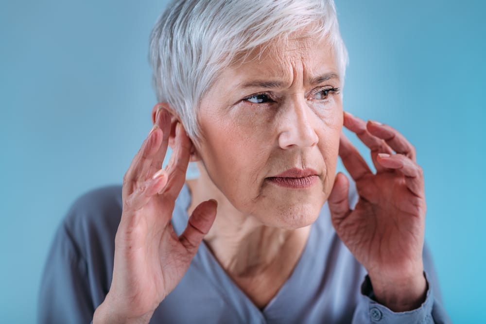 Senior woman touching her ears with the tips of her fingers, visibly concerned