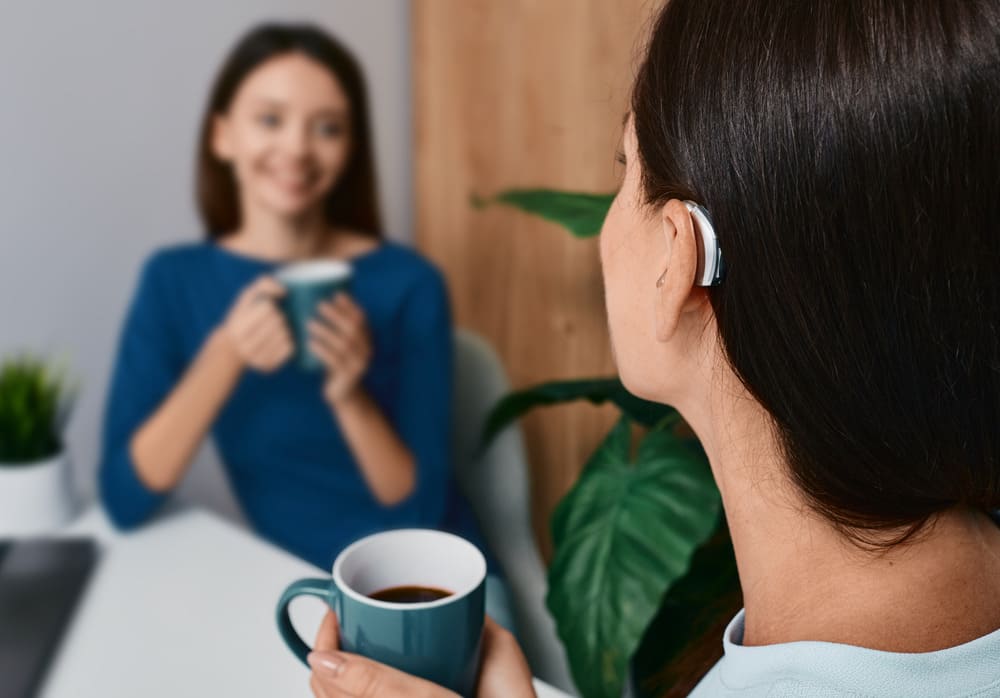Woman wearing a hearing aid having coffee with friend