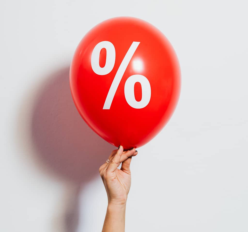 Photograph of red balloon with % sign on it being held against white background by feminine hand.