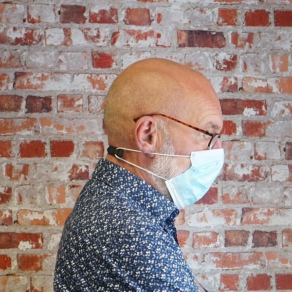 Man with facemask and ear protector standing infront of brick background